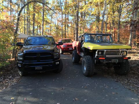 1979 Ford Bronco - A black Ram pickup truck is parked on a paved surface in front of a red pickup truck and a yellow and red custom off-road Ford Bronco. The…