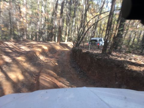 1979 Ford Bronco - A white SUV is seen driving on a dirt path through a forest. The vehicle is partially obscured by trees and the perspective is from inside…