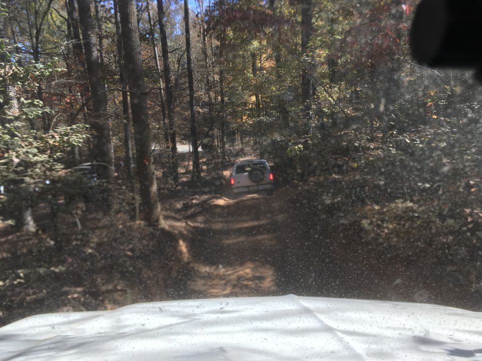 White SUV driving on a dirt road in a forest during autumn.