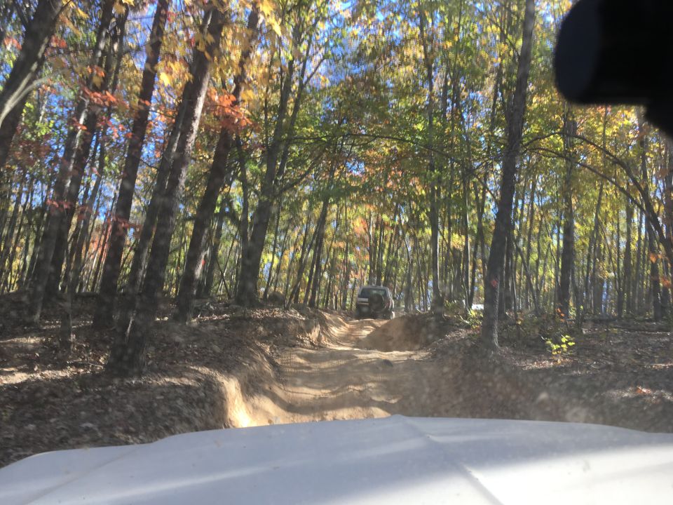 SUV driving up a dirt trail in an autumn forest.