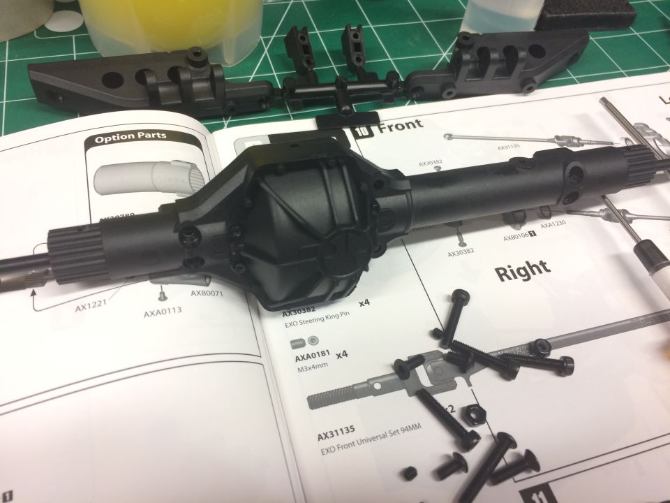 Black RC car axle assembly on instructions with scattered screws and nuts.