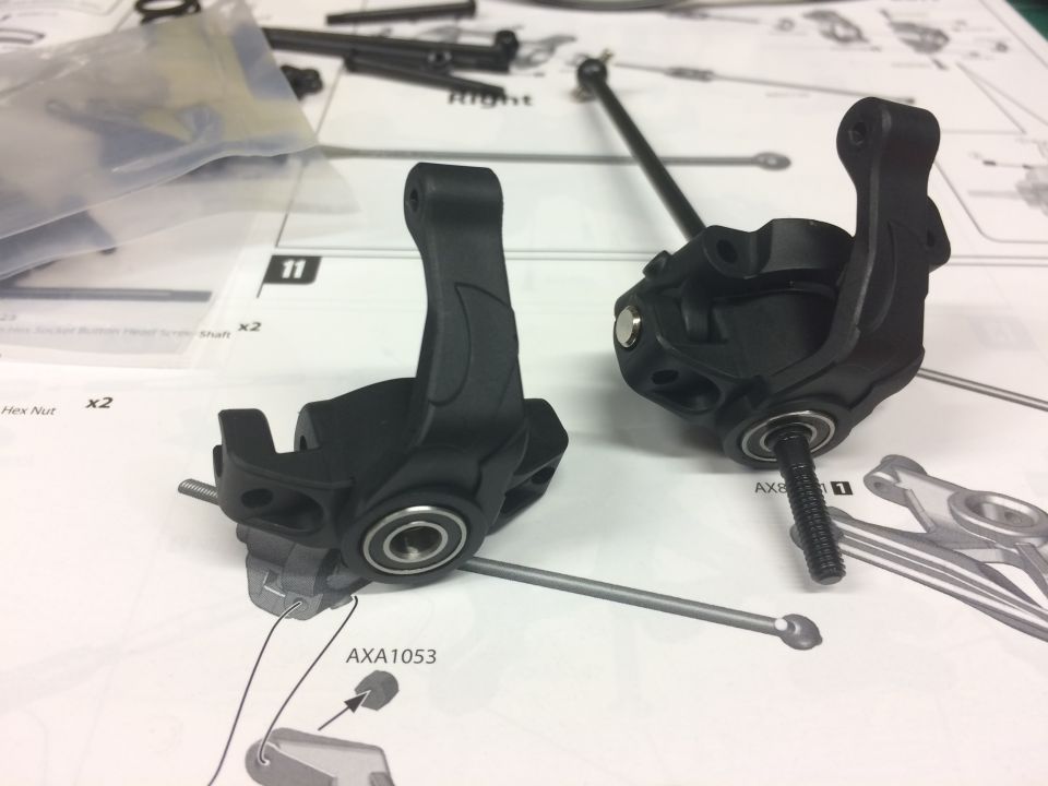 Two black RC car steering knuckles on an instruction manual.
