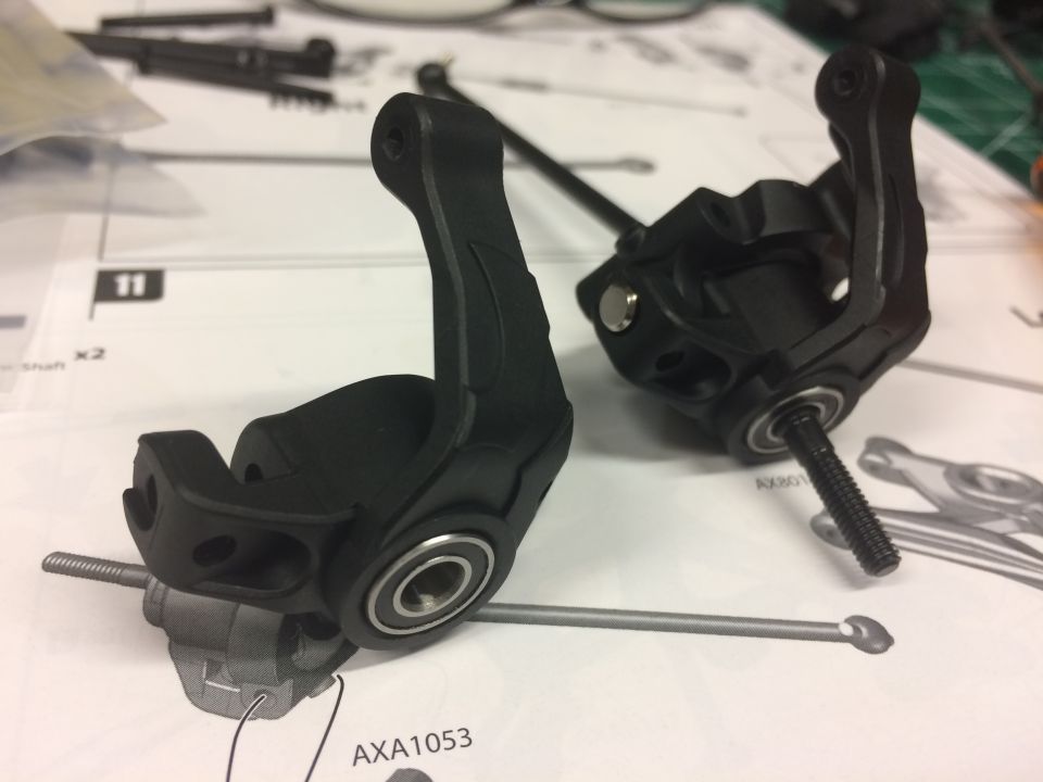Two black RC car steering knuckles with bearings and shafts on instructions.