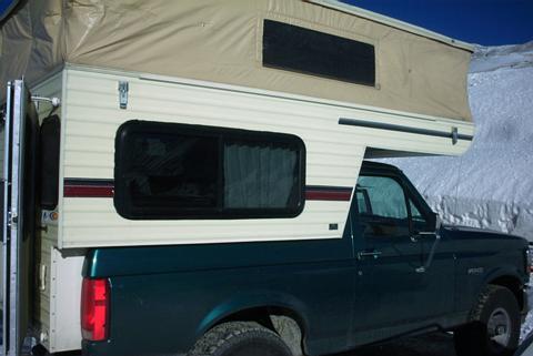 1995 Ford Bronco - A truck camper is mounted on a green pickup truck, seen from the front-right angle.