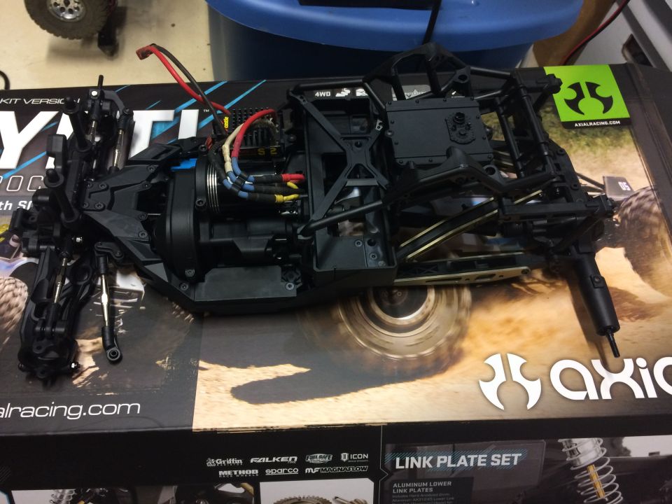 Black RC car chassis with wiring and motor on a box with Axial Racing branding.
