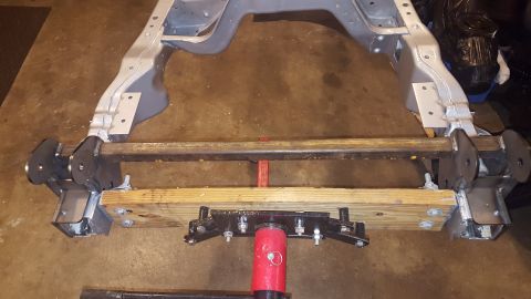 1994 Ford Bronco - A custom fabricated steel frame assembly, likely for a vehicle suspension, is supported by a hydraulic jack and wooden blocks on a concrete…