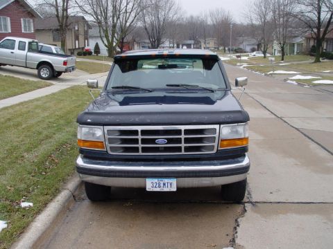 1995 Ford Bronco - Front view of a dark blue Ford F-Series truck, parked in a suburban driveway with another truck visible in the background.