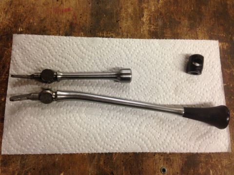 1979 Ford Bronco - Two chrome-plated levers with black grips and a small black cylindrical part are laid out on a white paper towel on a wooden surface.