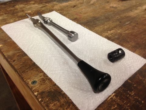 1979 Ford Bronco - Two metal levers with black handles and a black cylindrical part are laid out on a white paper towel on a wooden surface.