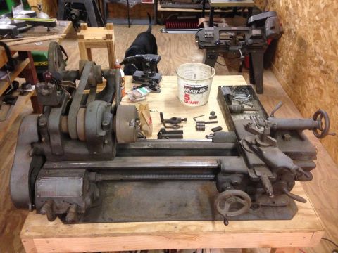1979 Ford Bronco - A metal lathe sits on a wooden workbench in a workshop. Various tools and a bucket are scattered around the machine.