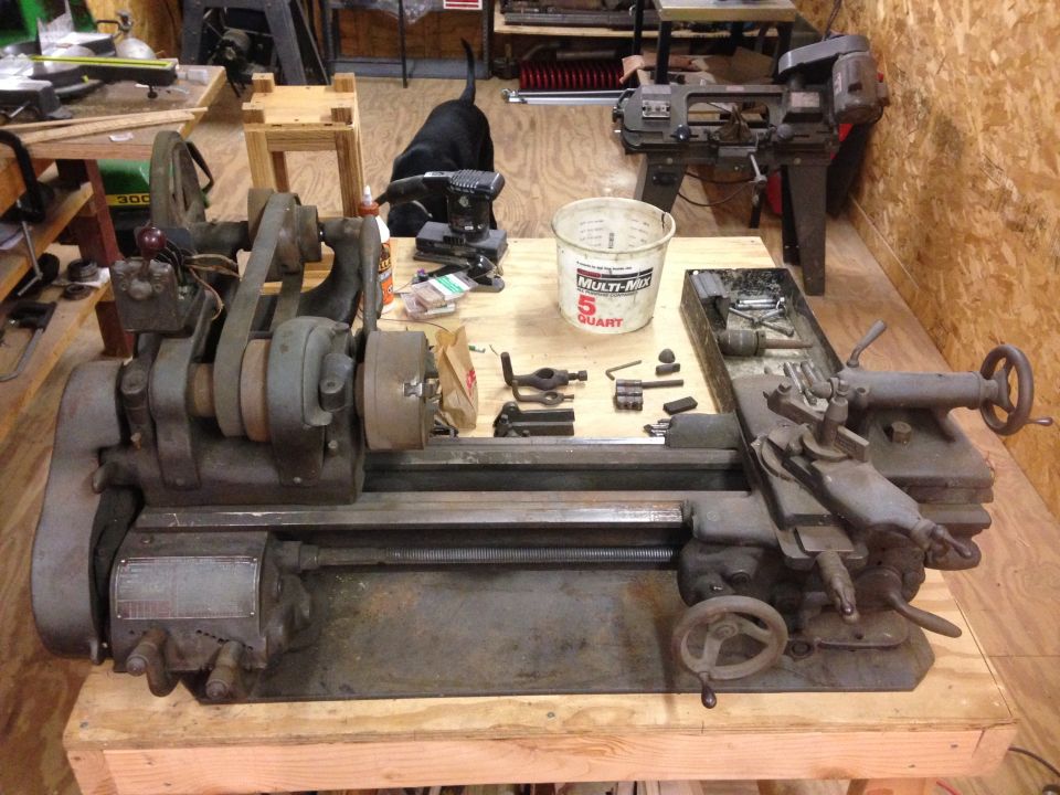 Metal lathe on a workbench in a workshop with tools and a bucket.