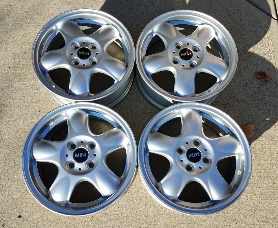 Four silver 5-spoke alloy wheels with black MINI center caps on concrete.