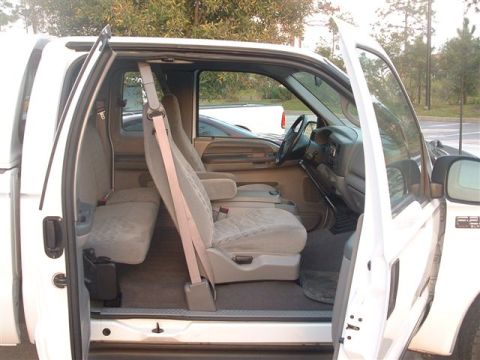 1986 Ford Bronco - The interior of a white pickup truck is visible with both front and rear doors open, revealing the seating arrangement.