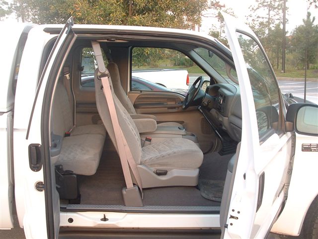Interior of a white pickup truck with open doors, showing front and rear seats
