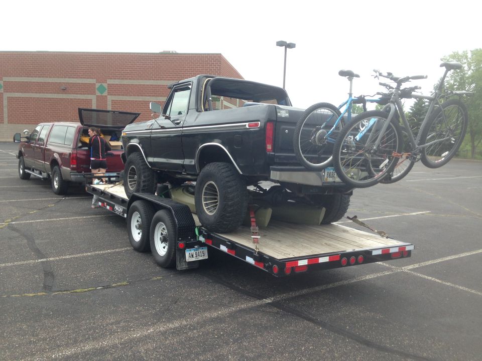 Black Ford Bronco on a trailer with bikes on the back, red Ford pickup in front.