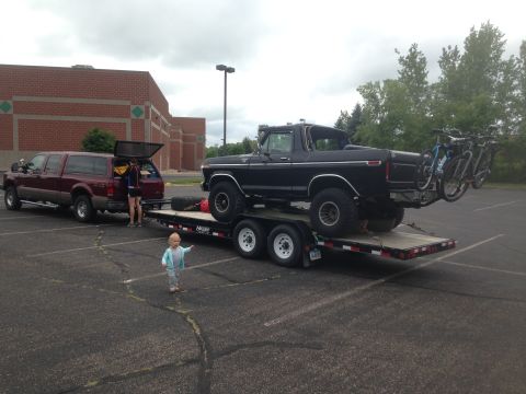 1979 Ford Bronco - A black Ford Bronco is loaded onto a flatbed trailer, with three bicycles mounted to its tailgate. A maroon Ford pickup truck is parked nex…