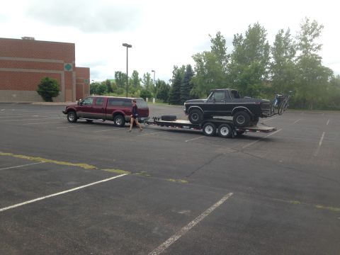 1979 Ford Bronco - A black Ford Bronco is loaded onto a flatbed trailer, which is being towed by a maroon Ford pickup truck. Two bicycles are mounted on a rac…