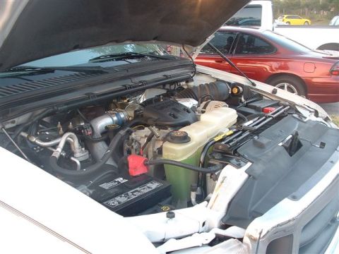 1986 Ford Bronco - The engine compartment of a white truck is shown with other vehicles visible in the background.