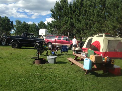 1979 Ford Bronco - A black 1979 Ford Bronco is parked on a grassy campsite next to a red truck and a large tent. Camping gear is spread out on a picnic table…