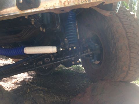 1979 Ford Bronco - The underside of a vehicle shows a blue shock absorber and a white and blue steering stabilizer. The vehicle's tire is resting on a large r…