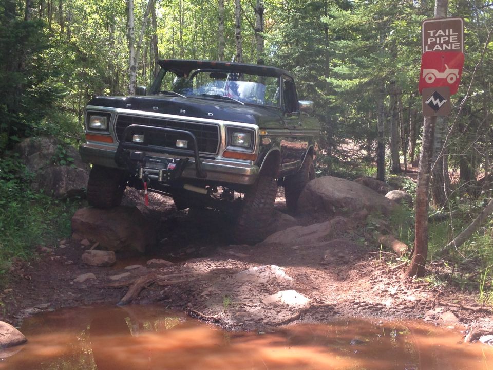 Black Ford Bronco off-roading on a muddy trail with a "Tail Pipe Lane" sign.