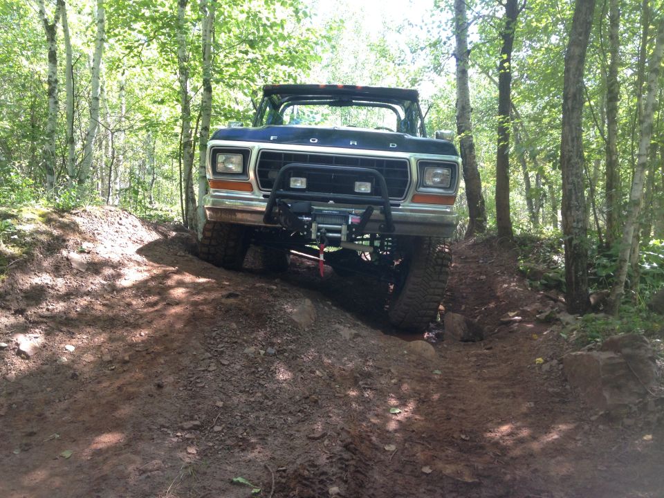 1979 Ford Bronco driving on a muddy trail in the woods.