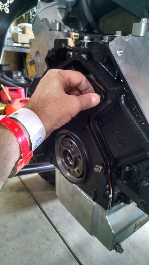 1985 Jeep CJ7 - A person's hand is shown installing a gasket onto the side of a black engine block. A silver oil pan is visible underneath the engine.