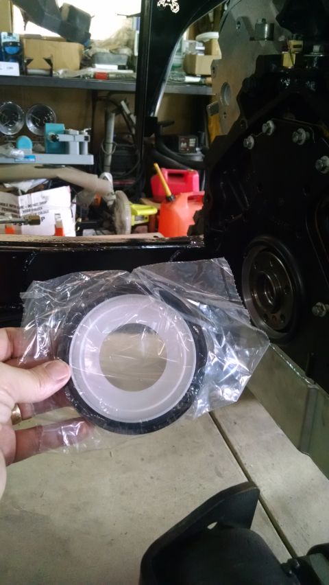 1985 Jeep CJ7 - A hand holds a new engine seal, still in its plastic packaging, in front of a black engine block in a garage setting. The engine appears to…