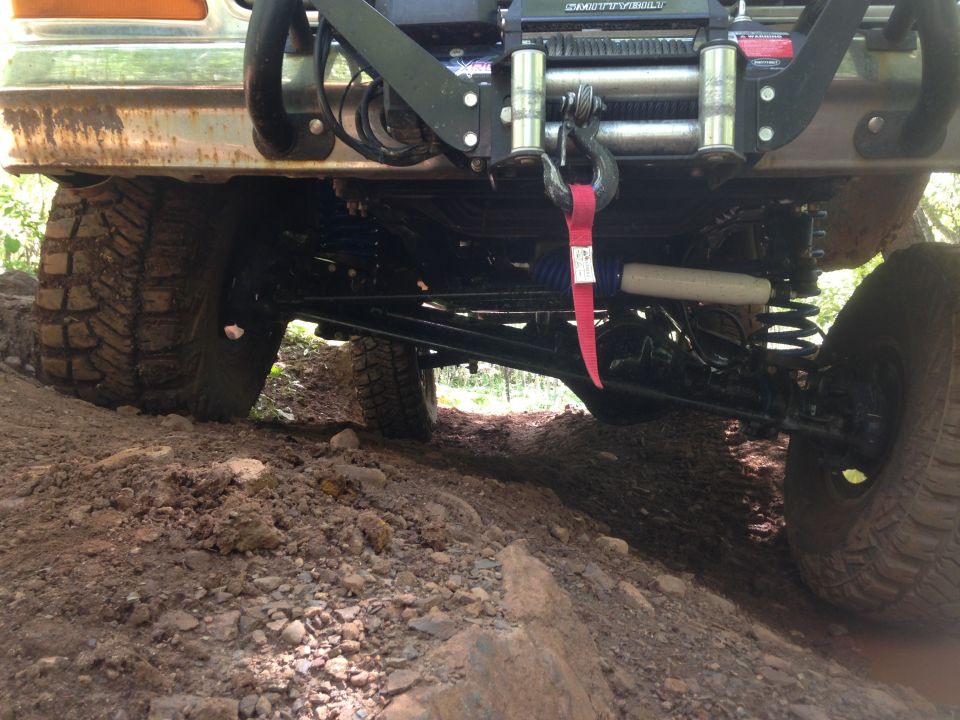 Rear underside of a lifted off-road vehicle on a dirt trail, showing winch and suspension.