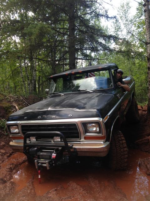 1979 Ford Bronco - A black 1970s Ford Bronco is shown off-road, stuck in deep mud with a winch mounted on the front bumper. A person is visible in the driver'…