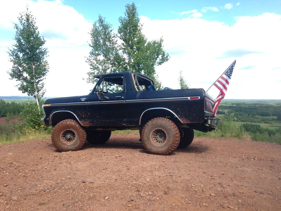 Black lifted 1979 Ford Bronco with American flag on a dirt hill.