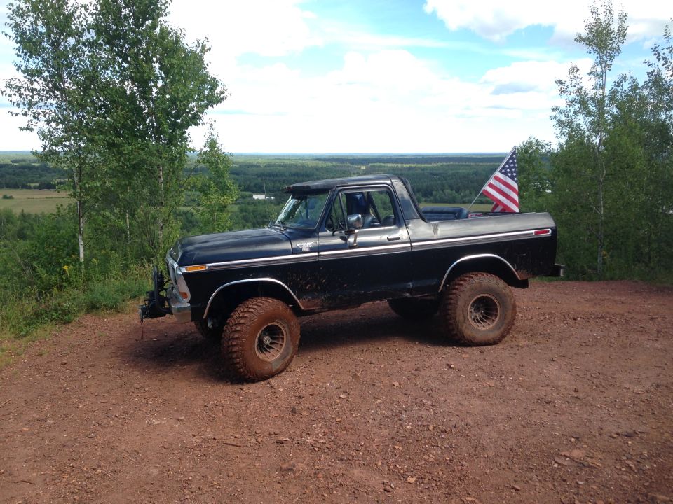 Black 1979 Ford Bronco parked on a dirt road with an American flag on the tailgate.