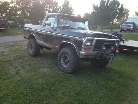 1979 Ford Bronco - A black 1979 Ford Bronco sits parked on a grassy area with a trailer and a newer model pickup truck visible in the background.