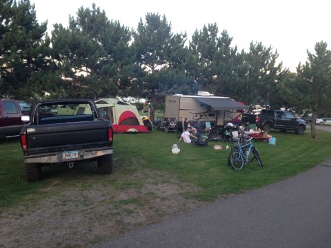 1979 Ford Bronco - A black Ford Bronco is parked on a grassy campsite next to a tent and a travel trailer. The Bronco is viewed from the rear, showing its lic…
