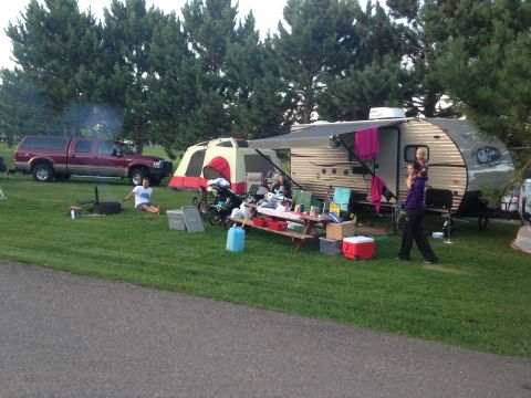1979 Ford Bronco - A red Ford F-Series pickup truck is parked next to a campsite with a travel trailer, tent, and picnic table. A man is sitting on the grass…