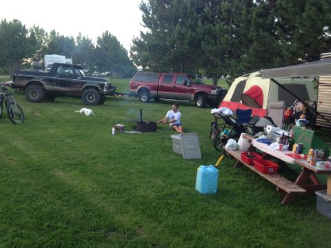 1979 Ford Bronco - A black 1979 Ford Bronco is parked on the grass next to a red pickup truck and a campsite with a tent and picnic table. A white dog is lyin…