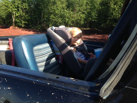 1979 Ford Bronco - A young child sits in a car seat in the back of a vintage convertible. The vehicle's interior features blue vinyl seats with a striped fabr…
