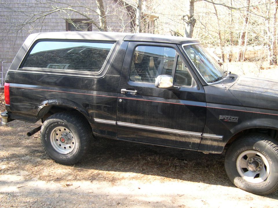 Black Ford Bronco SUV parked in side profile on dirt near a gray house