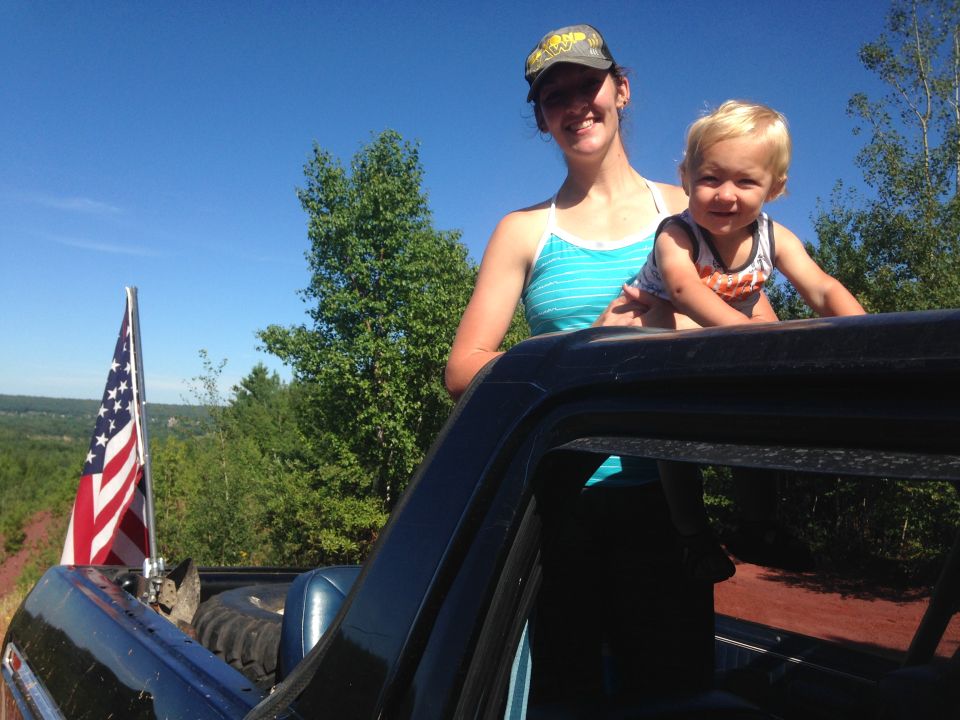 Woman and child in the bed of a dark pickup truck with an American flag.