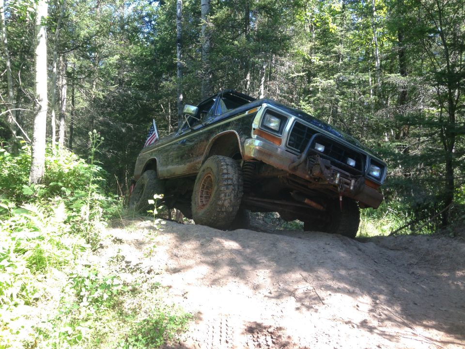 1979 Ford Bronco driving up a dirt hill in a forest.