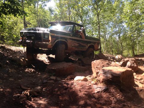 1979 Ford Bronco - A dark colored, lifted Ford Bronco is navigating a rocky, wooded trail with its front tires on large rocks. The vehicle appears to be a con…