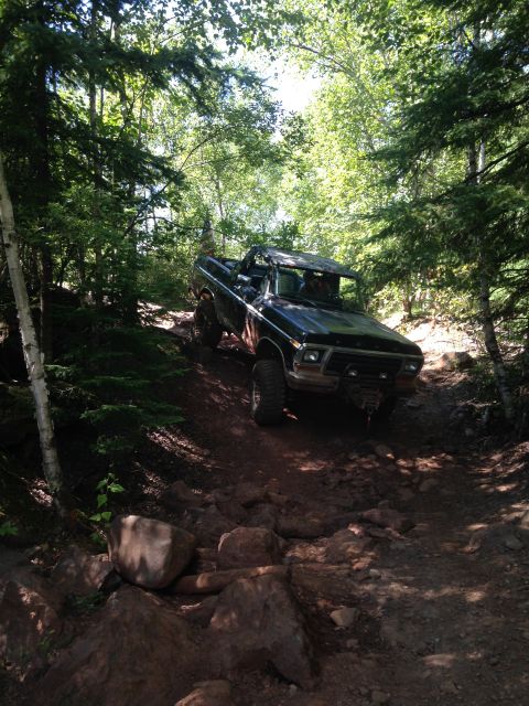 1979 Ford Bronco - A black 1979 Ford Bronco is navigating a rocky, wooded trail. The top is off the vehicle, and it appears to be a sunny day with dappled lig…