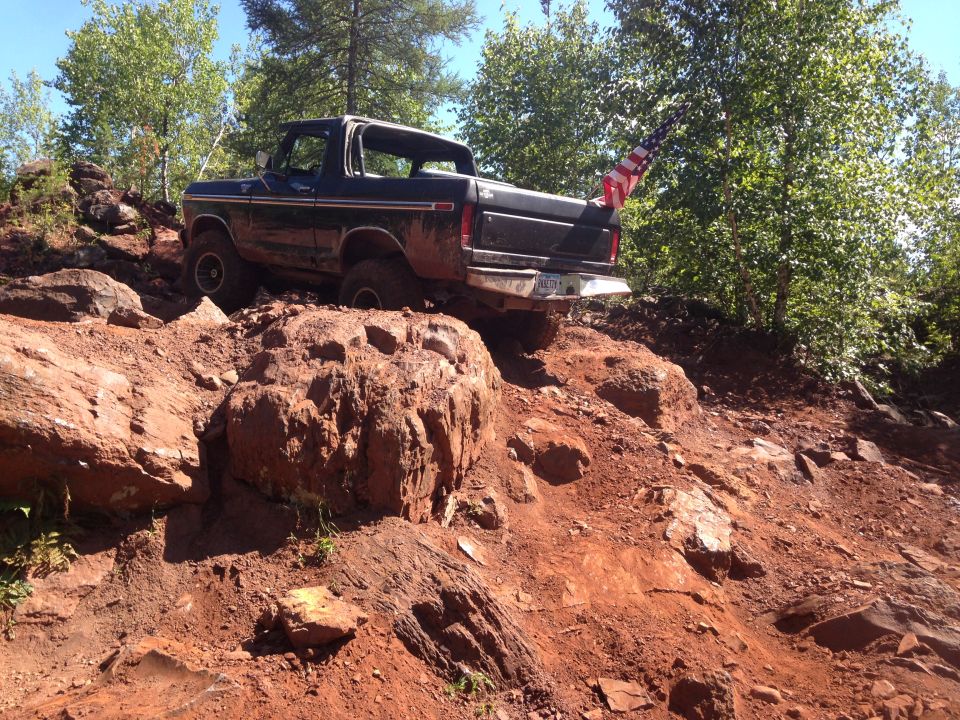 Dark-colored 1979 Ford Bronco navigating a steep, rocky, and muddy off-road trail.
