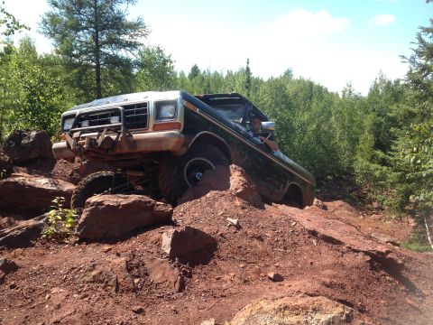 1979 Ford Bronco - A dark green Ford Bronco is navigating a steep, rocky, off-road trail with a person visible in the driver's seat. The vehicle has a promine…