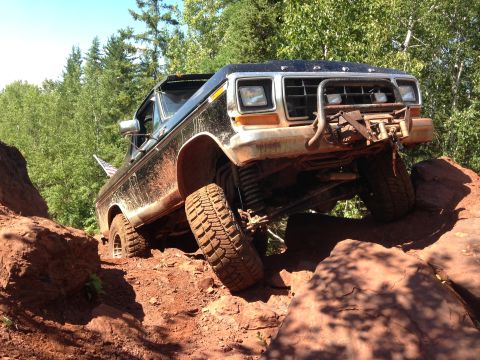 1979 Ford Bronco - A black 1979 Ford Bronco is navigating a rocky, off-road trail with its front tires elevated on large red rocks. The vehicle is equipped wi…