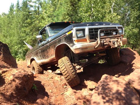 1979 Ford Bronco - A black 1979 Ford Bronco is shown off-roading over large rocks and dirt. The vehicle has a lifted suspension and an aftermarket front bumpe…