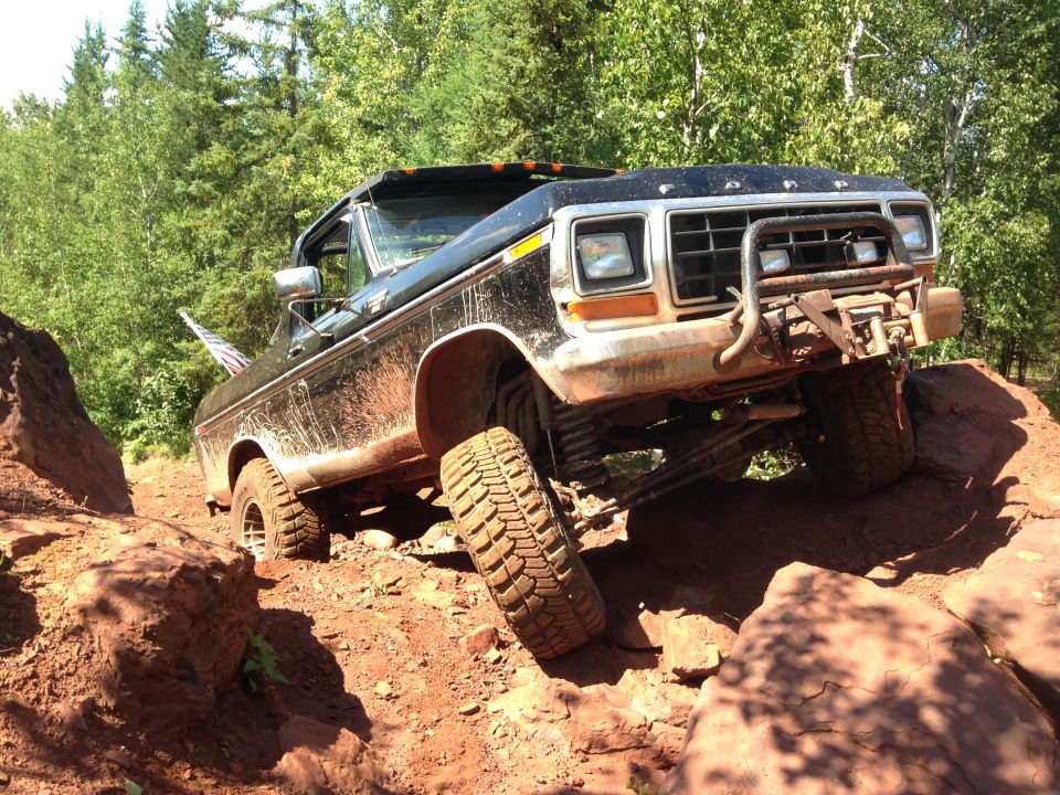 1979 Ford Bronco off-roading over rocks, lifted suspension, aftermarket bumper with winch