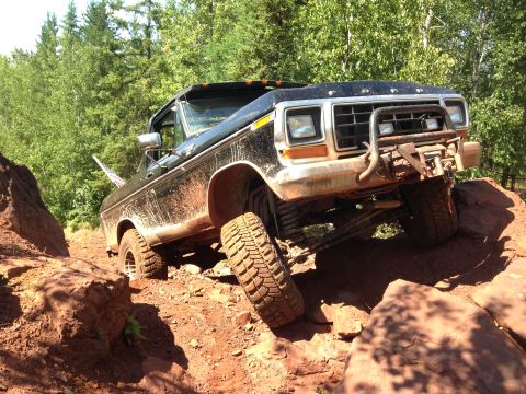 1979 Ford Bronco - A black 1979 Ford Bronco is navigating a rocky, off-road trail with significant articulation in its suspension. The vehicle is covered in m…