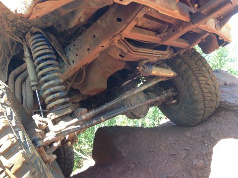 1979 Ford Bronco - Underside view of a lifted 4x4 vehicle, likely an SUV or truck, navigating over large rocks. The suspension components, including a coil sp…