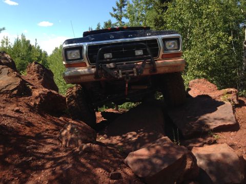 1979 Ford Bronco - A black 1979 Ford Bronco is navigating a rocky, off-road trail with a winch mounted on the front bumper. The vehicle is angled upwards, wit…
